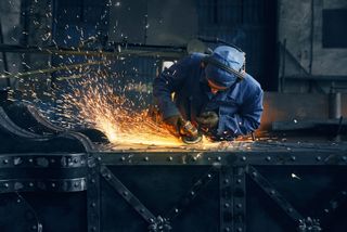 Industrial worker generating sparks while grinding metal, wearing Alsico protective workwear.