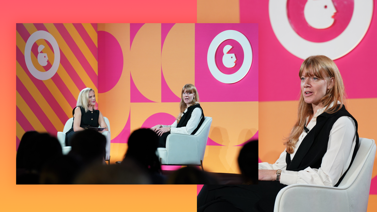 Two women sitting on stage talking, with bright orange and pink geometric shapes in the background