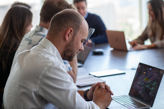 A group of people in a meeting board, one laptop has Atlassian's project board on the screen.