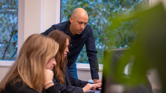 The team in EMEA work in their office Dom looks over another's shoulder at the computer.