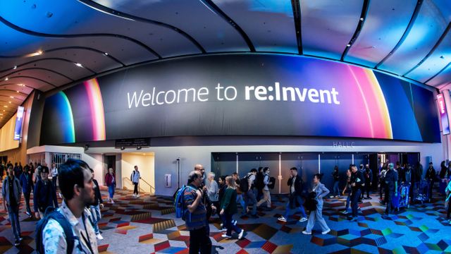 A bustling crowd walks under a large "Welcome to re:Invent" sign in a colorful, modern convention hall.
