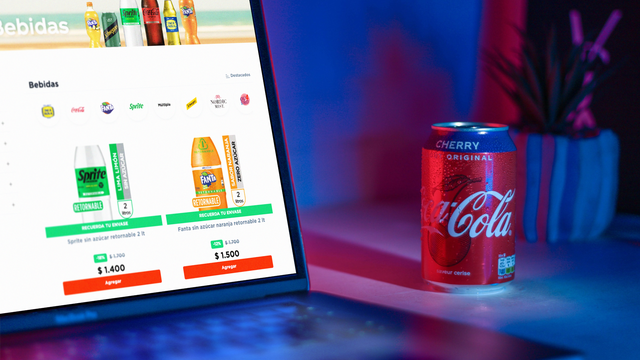 A laptop shows the Coca-Cola Embonor website. A cherry cola sits on the desk next to the laptop.