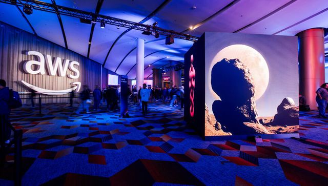 People at a tech event with large screens displaying the AWS logo and a lunar landscape under purple lighting.