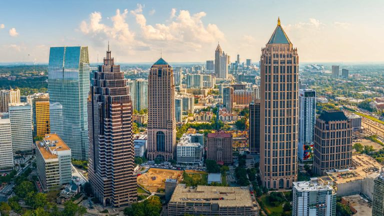 Aerial view of Atlanta's skyline with tall skyscrapers, including glass and brick buildings, under a partly cloudy sky.