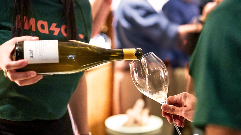 A server wearing a green Masal uniform is pouring some wine to another person's glass