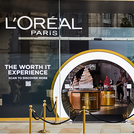 Storefront of L'Oréal Paris with "The Worth It Experience" display featuring beauty products, a QR code, and a circular entrance.
