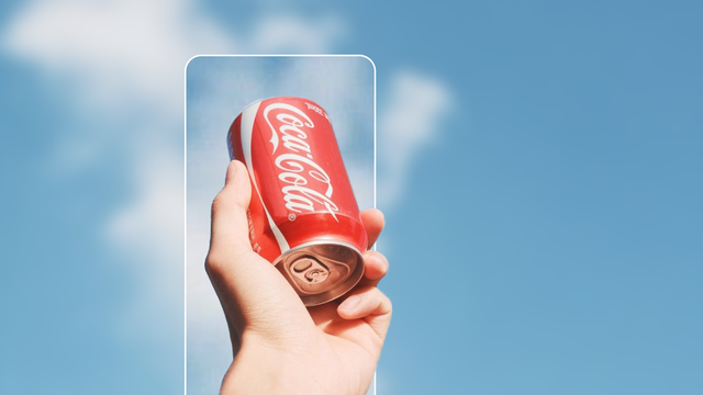 A hand holding an upside down Coca Cola bottle against a light blue sky