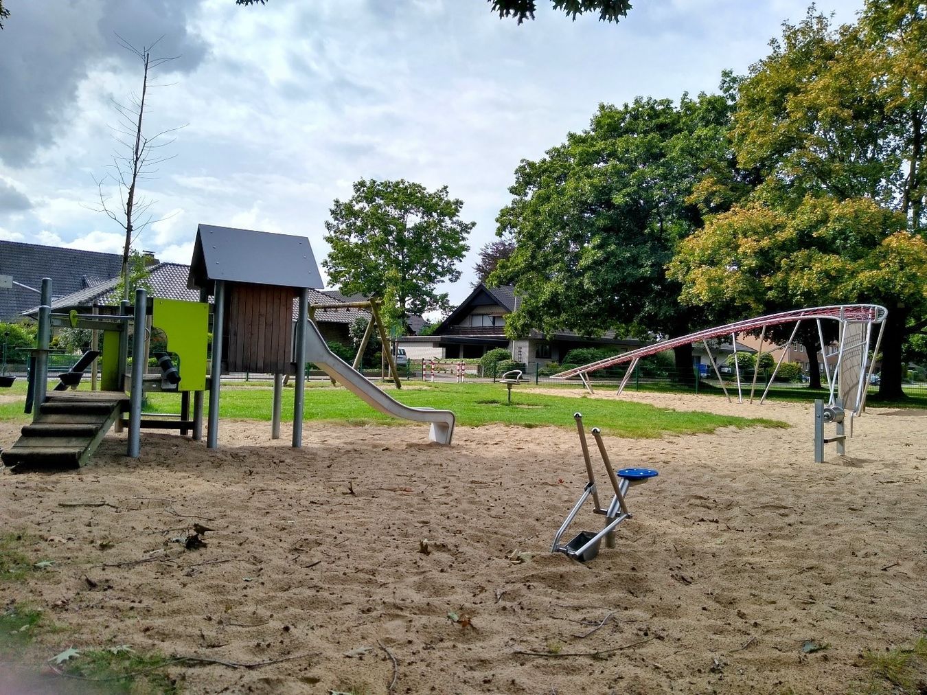 Abbildung eines Spielplatzes. Kleiner Turm mit Rutsche links. Klettergerüst rechts. Boden aus Sand und Gras