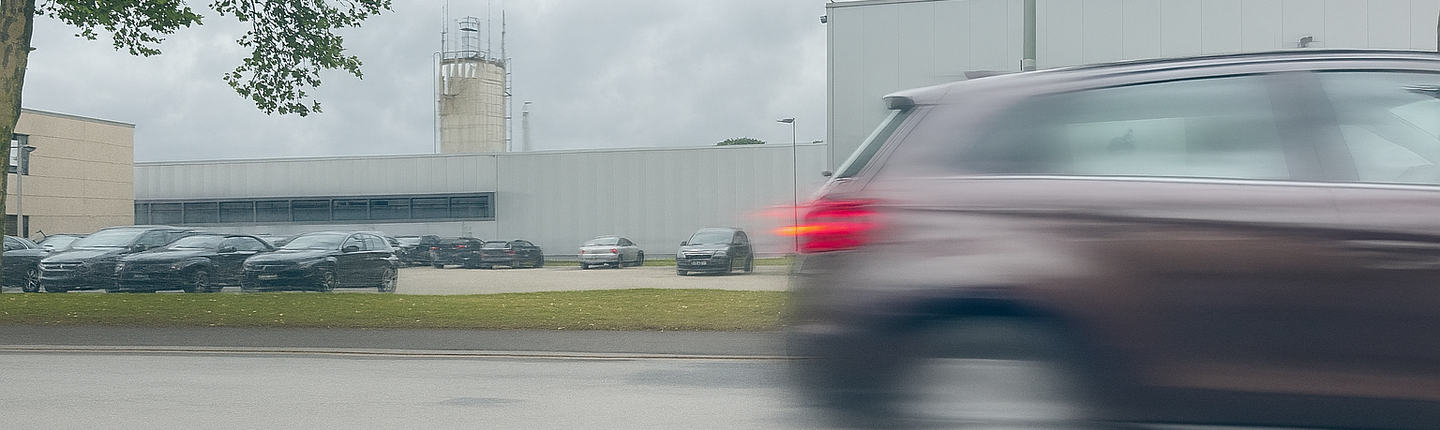Verschwommenes Heck eines Autos vor dem Industriegebiet.