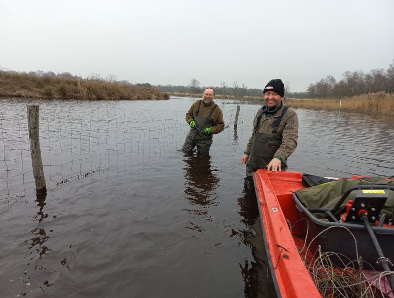 Zwei Perosnen stehen Knietief neben einem Boot im Wasser.