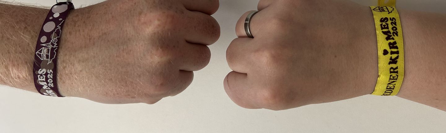 Zwei Arme, die jeweils eine Faust bilden, gegenüber. Dabei trägt jeder Arm jewils eins der beiden Alterkontrollbändchen.