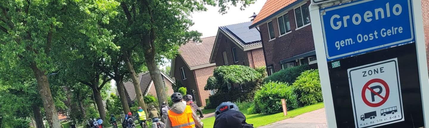 Kinder auf Fahrräder in einer Reihe fahren am Ortsschild Gronloe vorbei