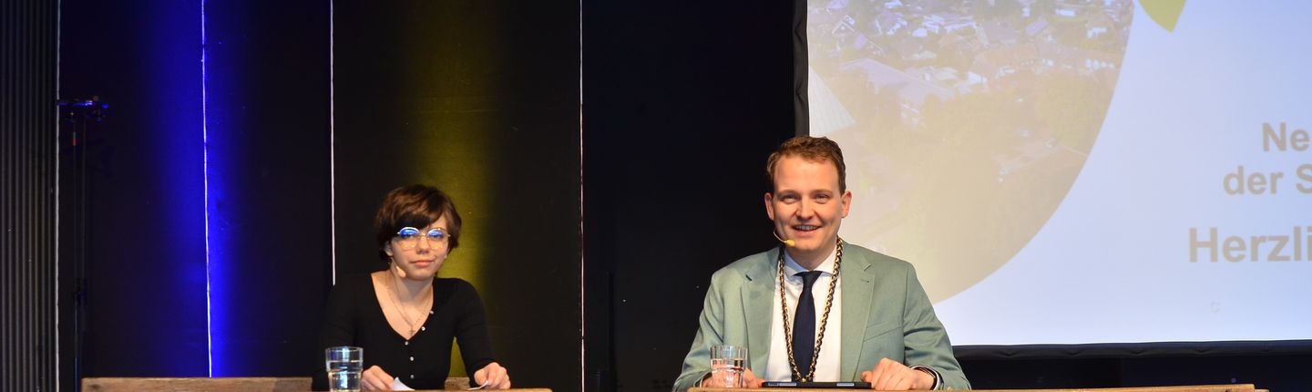 Leyla Mende und Bürgermeister Dr. Tom Tenostendarp gemeinsam auf einer alten Schulbank.