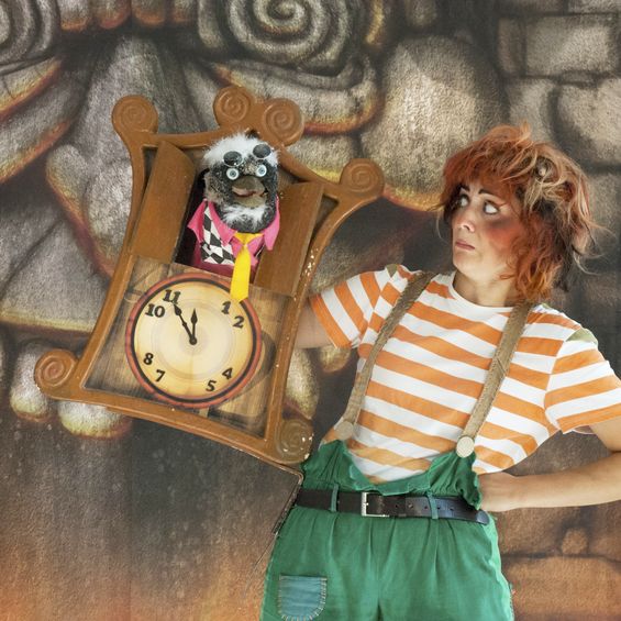 Aufnahme aus dem Theaterstück "Der kleine Zahlenteufel. Der Zahlenteufel schaut aus einer Kuckucksuhr. Eine Frau in Orange-weiß gestreiftem T-Shirt schaut ihn an.