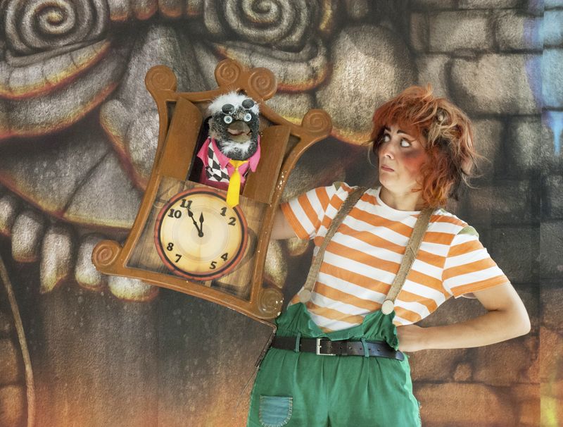 Aufnahme aus dem Theaterstück "Der kleine Zahlenteufel. Der Zahlenteufel schaut aus einer Kuckucksuhr. Eine Frau in Orange-weiß gestreiftem T-Shirt schaut ihn an.