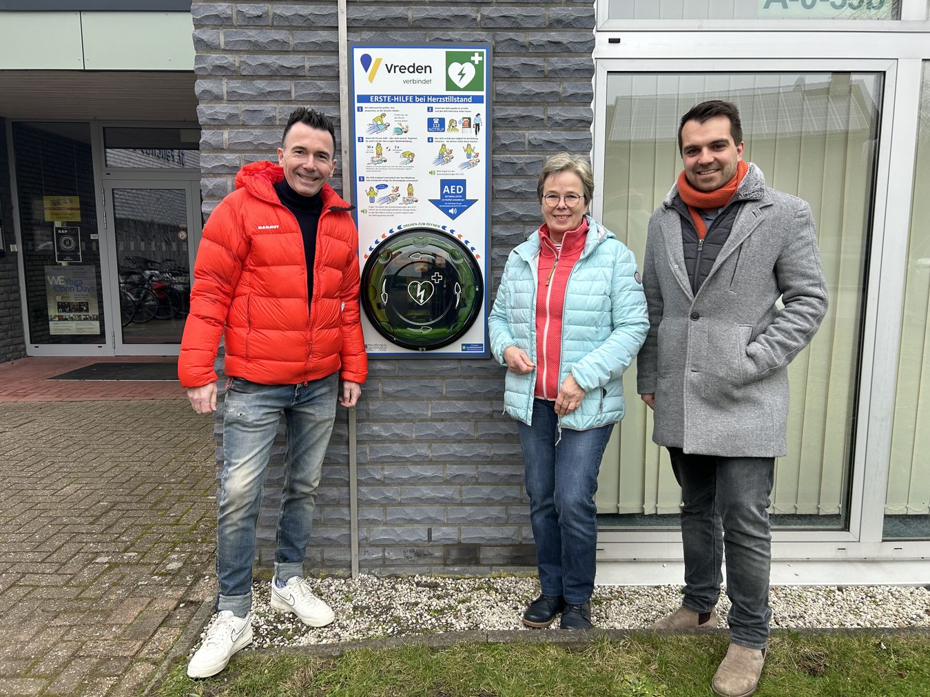 Der neue Defibrillator an der St.-Felicitas-Schule mit (v. l.) Sven Kruse, Schulleiter der St. Felicitas-Schule, Elisabeth Ingenhorst (Vorsitzende des Ausschuss für Soziales, Gesundheit, Generationen und Ehrenamt) und Fadi Rajab, Erster Beigeordneter der Stadt Vreden.