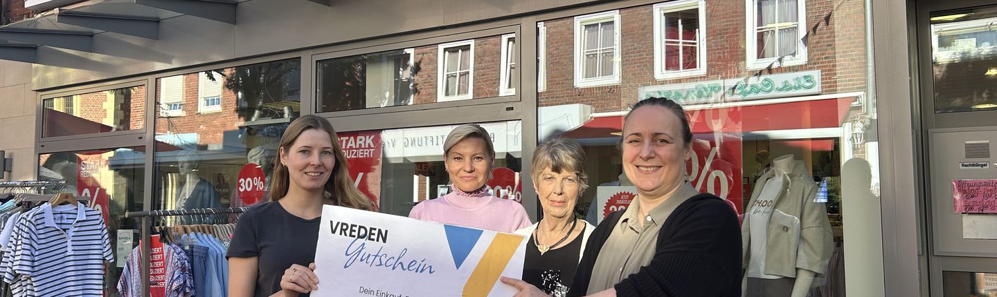 Mitarbeitende des Stadtmarketings und von Mode am markt vor dem Geschäft, einen großen Vreden-Gutschein in den Händen.