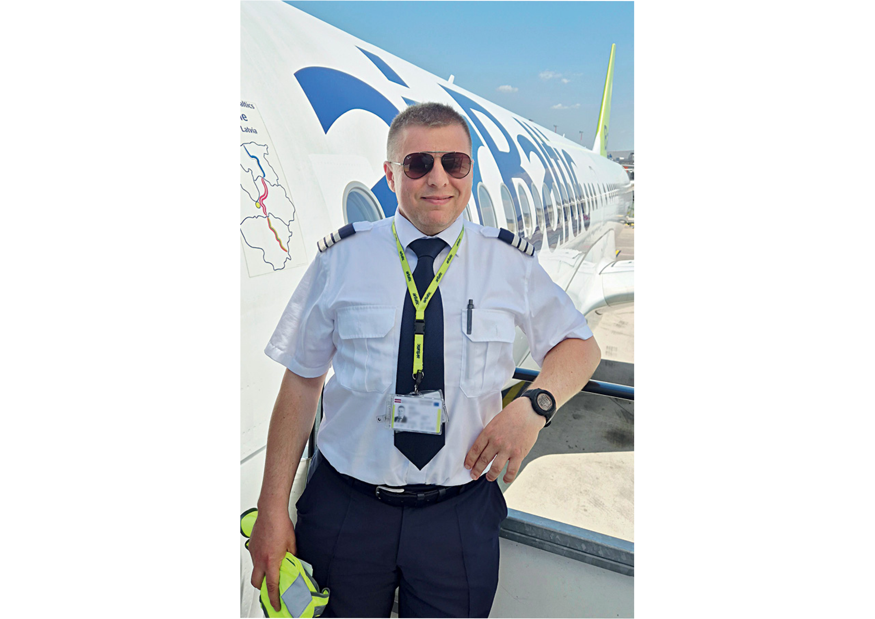 Jens Matthias Balasch Pilot in uniform standing beside an airBaltic airplane, smiling and wearing sunglasses.