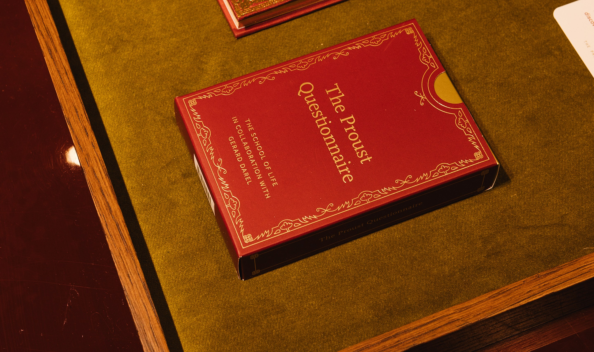 A red book titled "The Proust Questionnaire" rests on a textured green surface with a wooden border.