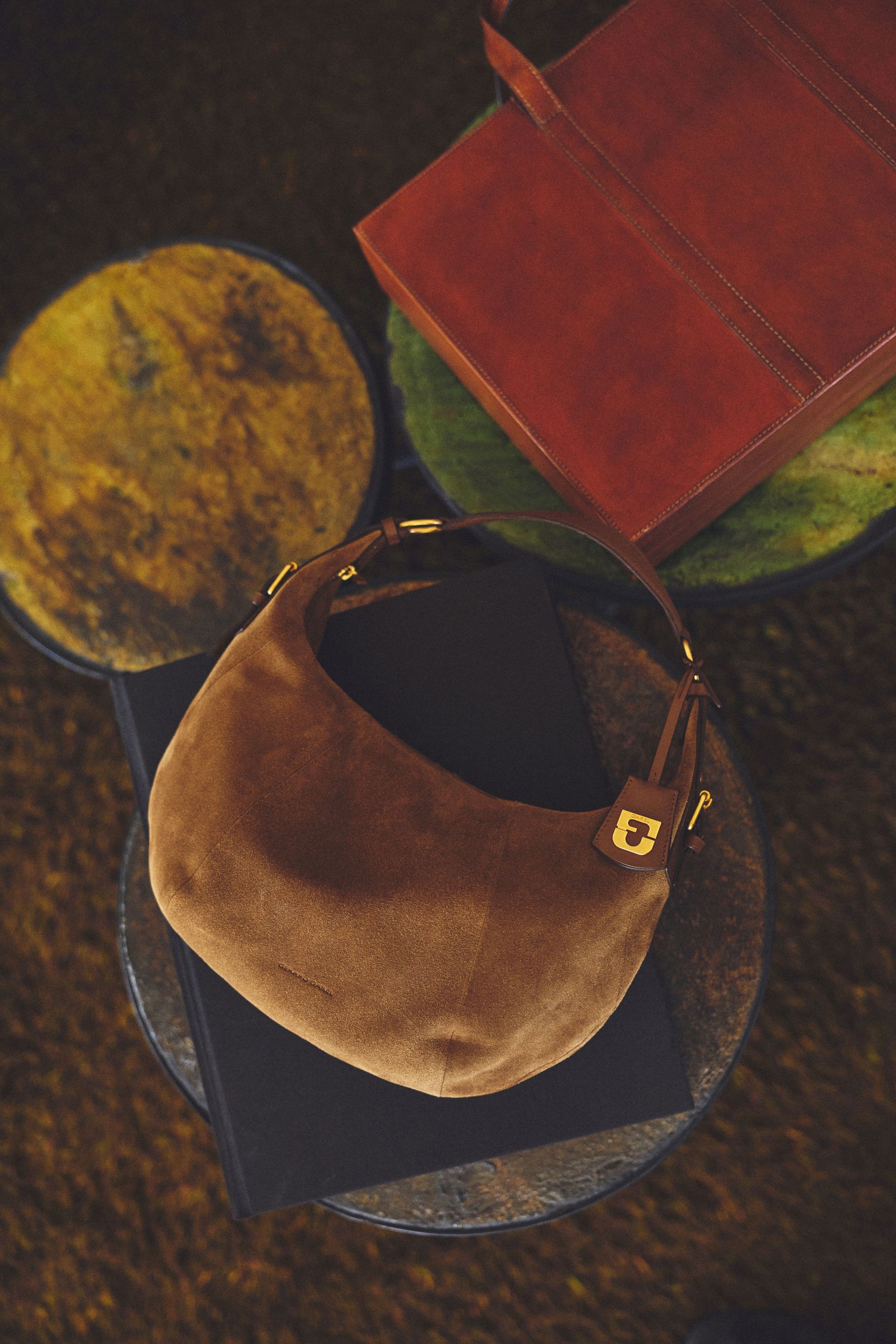 Brown suede handbag with gold accents on top of two round, textured stools and a leather folder.