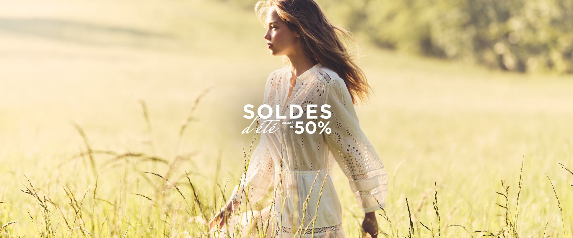 A woman in a white dress walking through a sunny field, with text overlay "SOLDES d'été -50%" indicating a summer sale.
