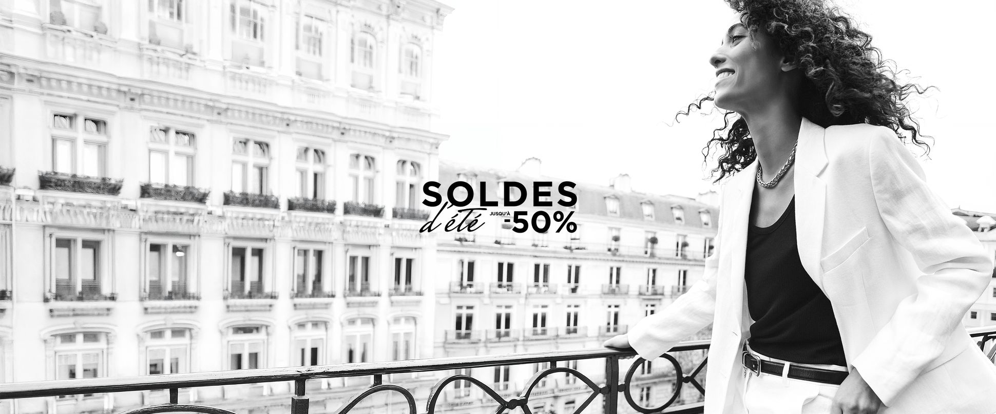 Woman in a white suit smiling on a balcony with "Soldes d'été -50%" text. Parisian building facade in the background.