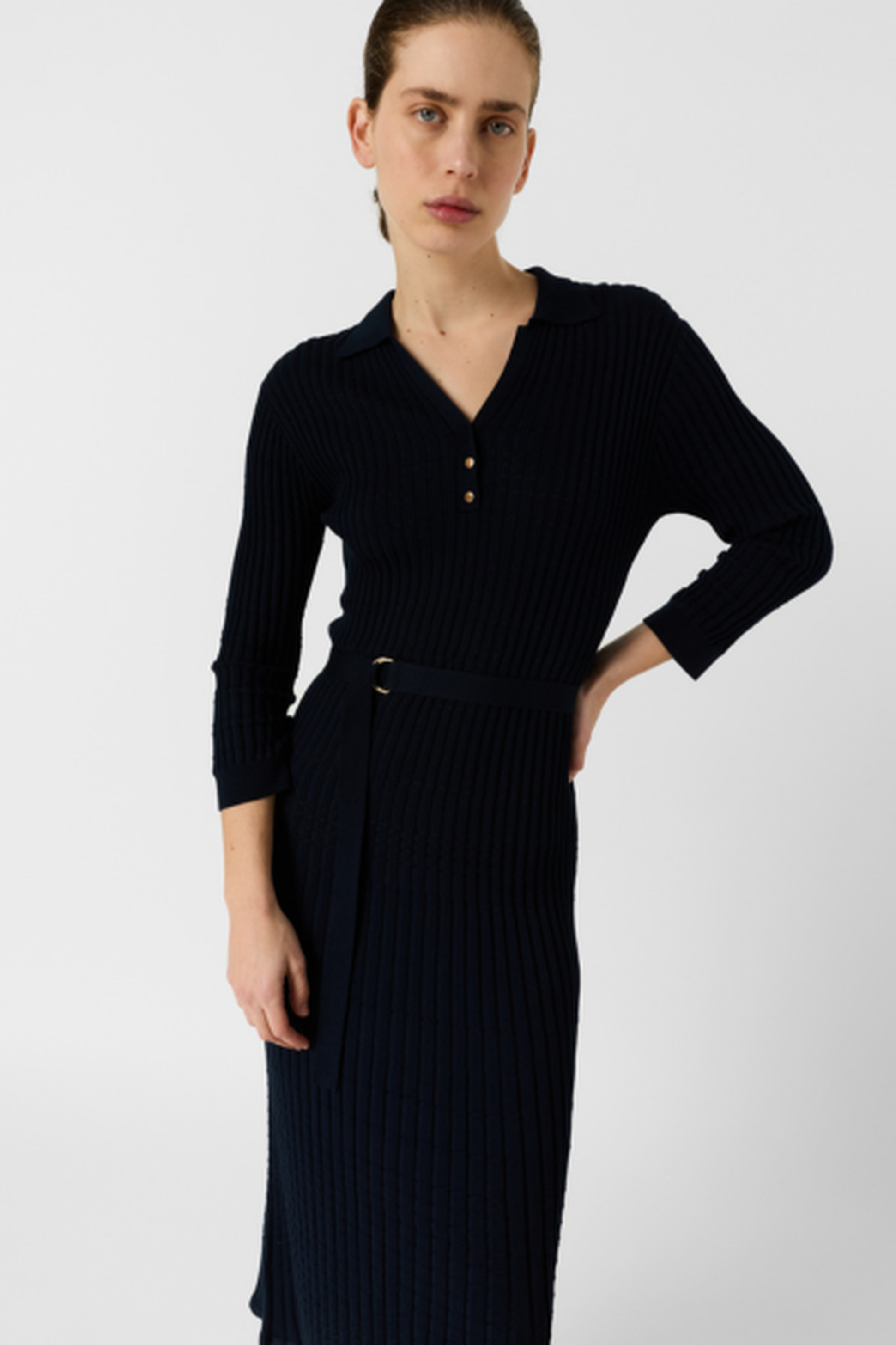 Person in a ribbed navy dress with a belt and three-quarter sleeves, standing against a plain background.
