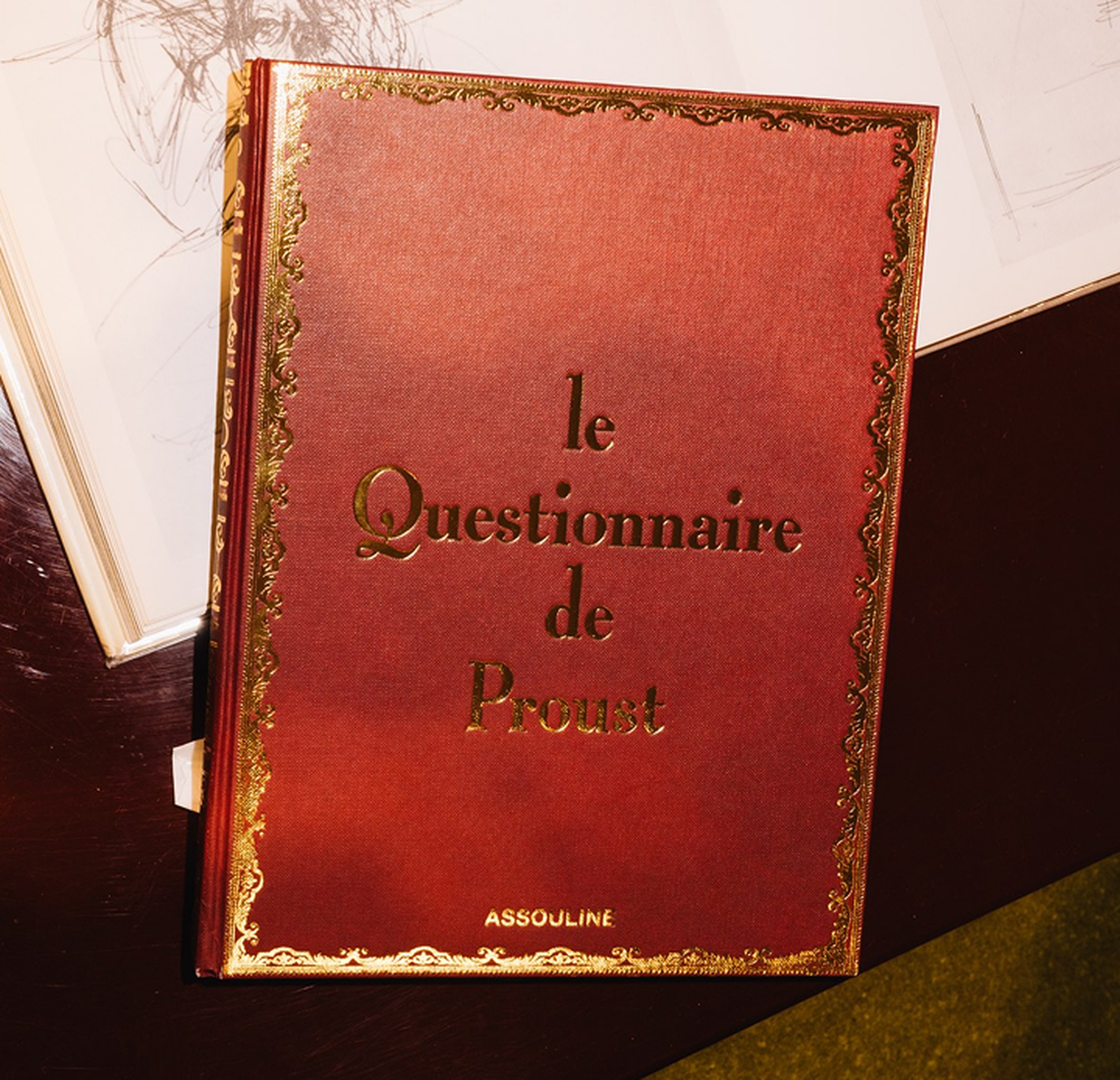 A red book titled "Le Questionnaire de Proust" with gold decorative borders and lettering, published by Assouline.
