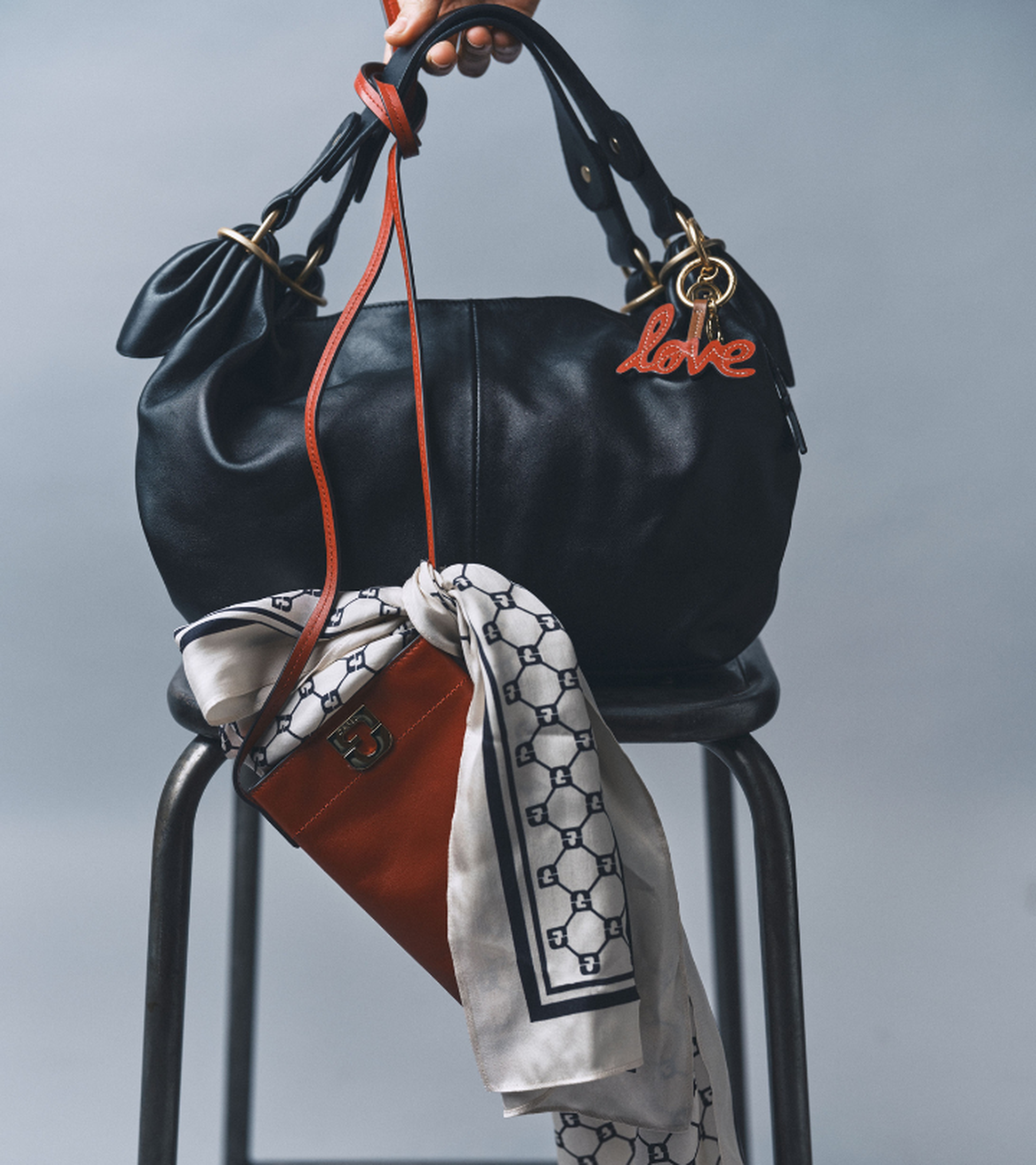 A black handbag with a "love" keychain, a patterned scarf, and a small red purse, all draped over a metal chair.