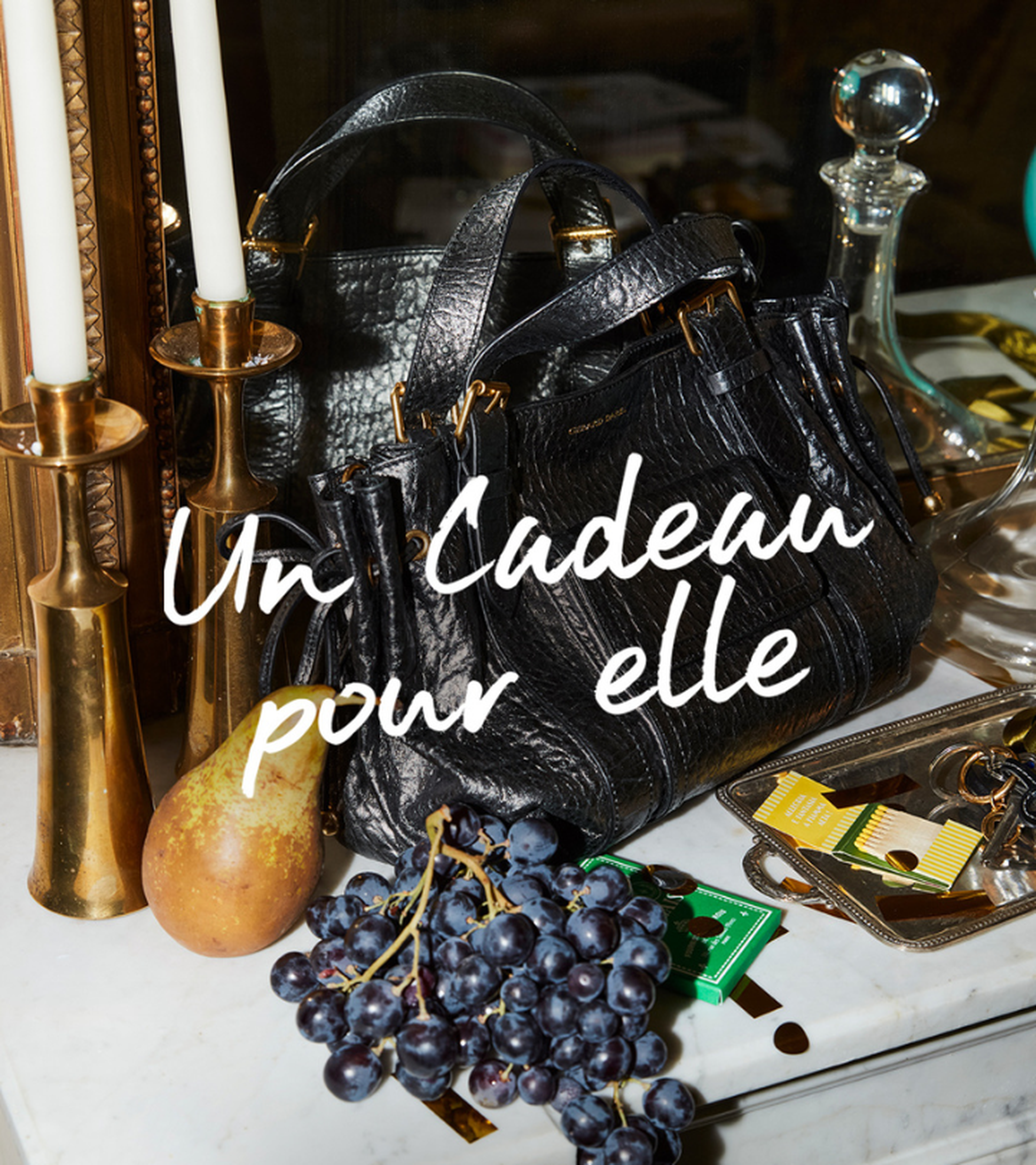 a black bag siting on a marble vanity with grapes and candles