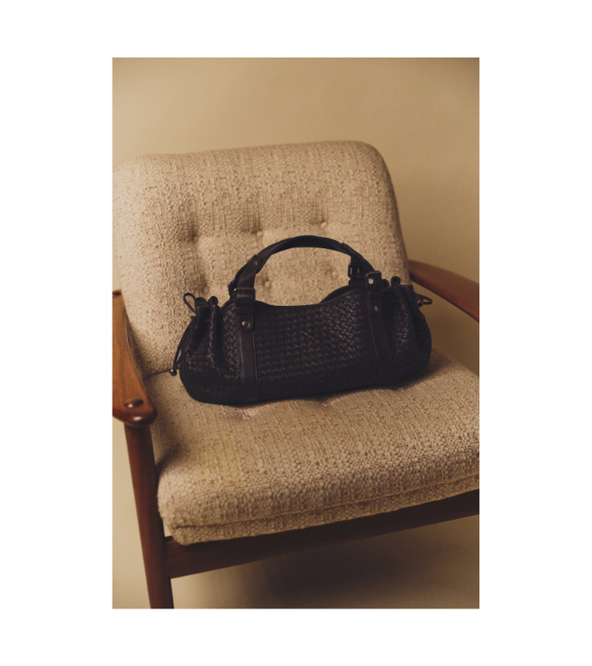 Woven black leather handbag on a beige, mid-century modern chair.