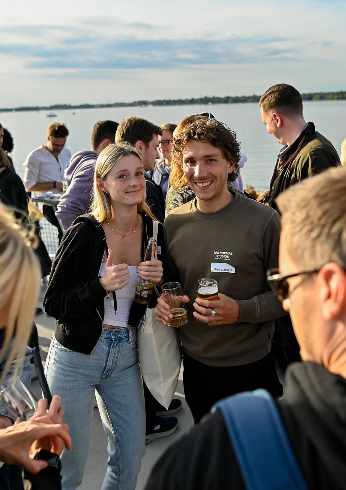 Maria und Julian lächeln mit Getränken auf einem Boot.