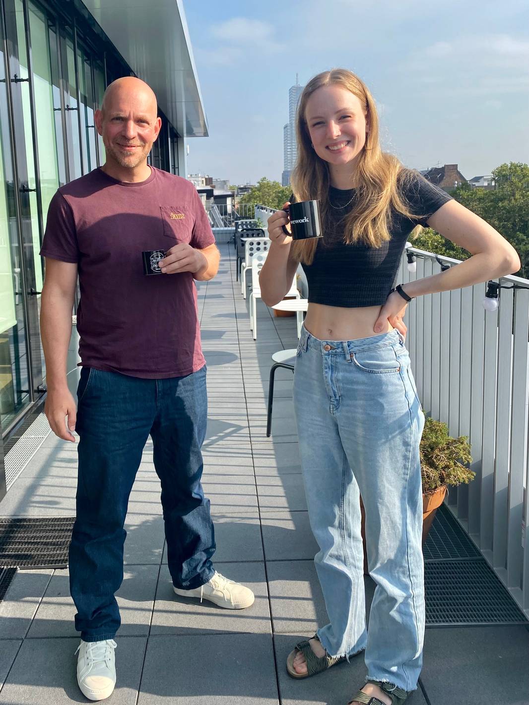 Kostas und Marieke lächeln auf der WeWork-Dachterrasse mit Tassen in der Hand.