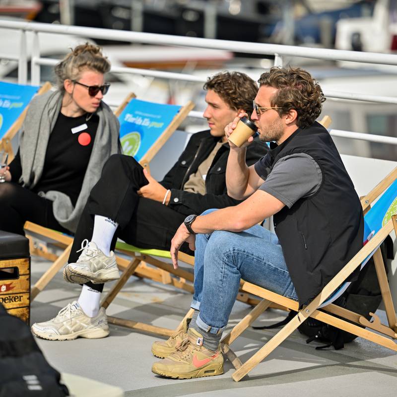 Elin, Julian und Philipp sitzen nebeneinander auf Strandstühlen. Elin schaut zu Julian, während Philipp rechts sitzt und einen Kaffee trinkt.