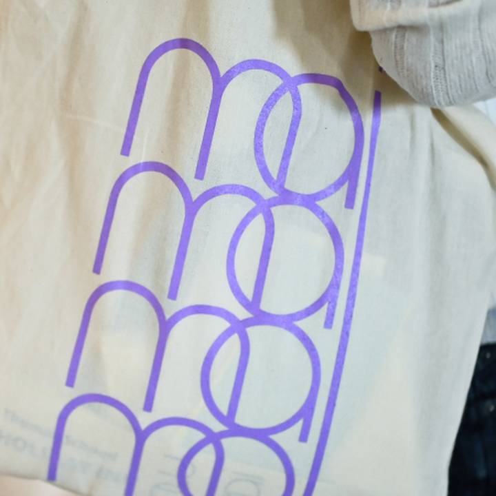 Auf einer hellen Stofftasche ist das Mai-Group-Logo viermal in lila übereinander aufgedruckt.