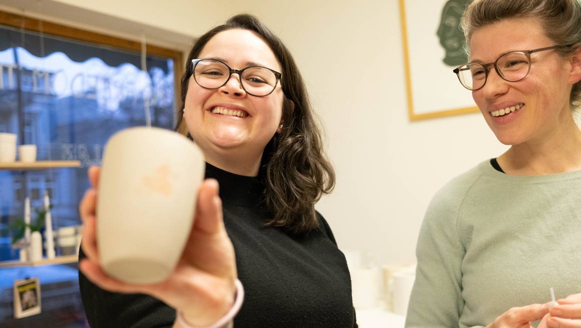 Natali und Elin lachen, Natali zeigt ihre getöpferte Tasse.