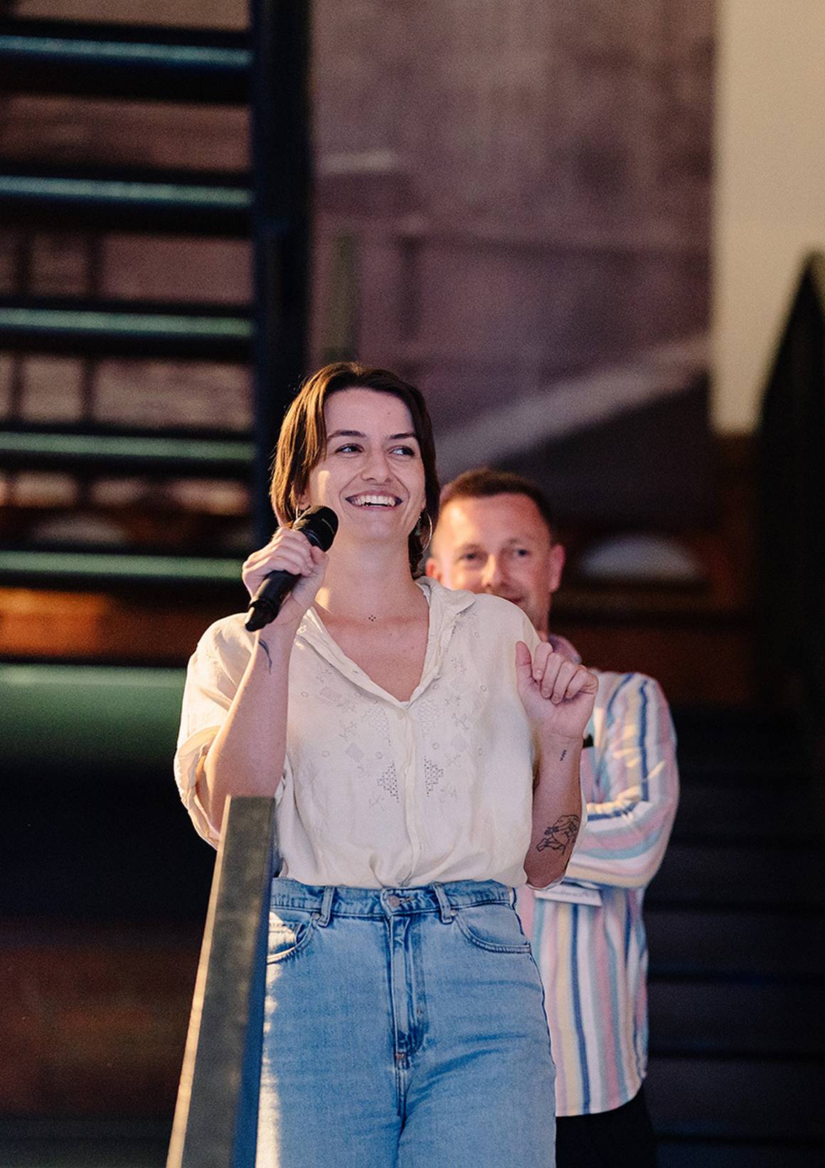 Vanessa spricht ins Mikrofon, Philipp lächelt neben ihr.