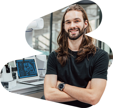 optician wearing a black tshirt and crossing his arms sitting in his lab with his desk in the background