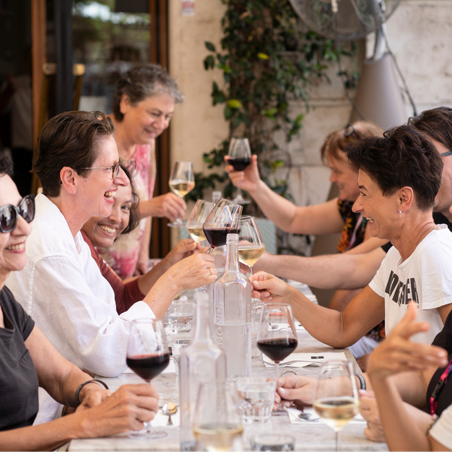 A group of adults seated at an outdoor table raising glasses of wine together during a meal.