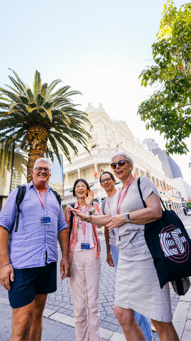 Four adults walking together on a sunny city street with a palm tree and historic building in the background.