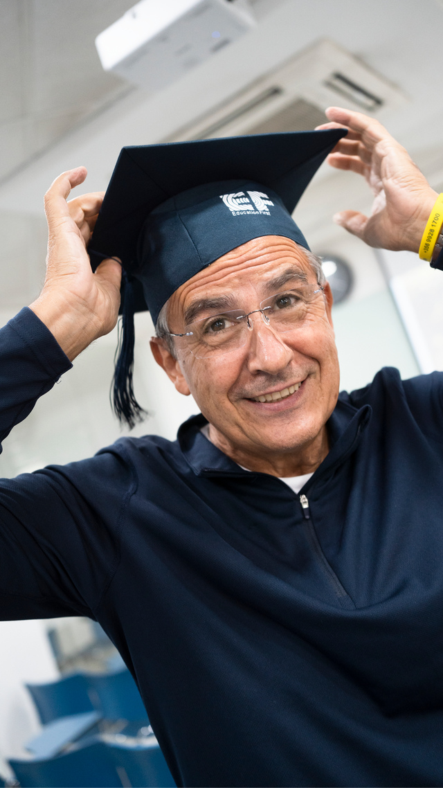 A man placing an EF graduation cap on his head and smiling in a bright indoor setting.