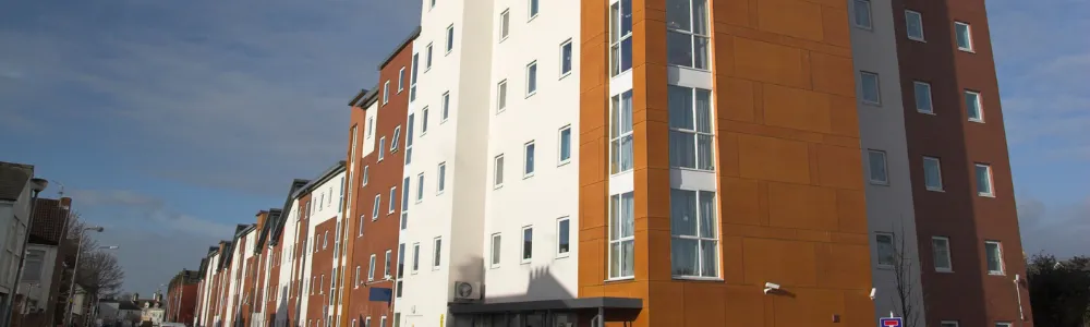 Modern multi-story buildings with large windows, situated on an urban street under a blue sky.