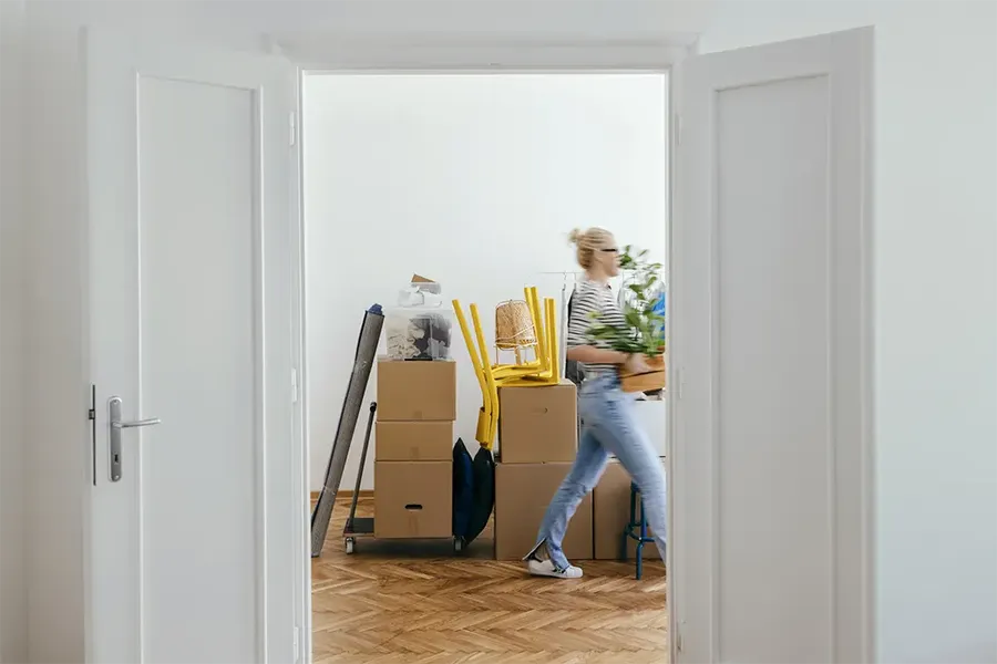 woman walking in hallway of new home carrying a plant with boxes stacked behind her