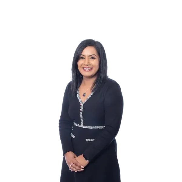 Arti Dhamu standing and smiling with long black hair in a black dress with silver trim, with a plain white background.