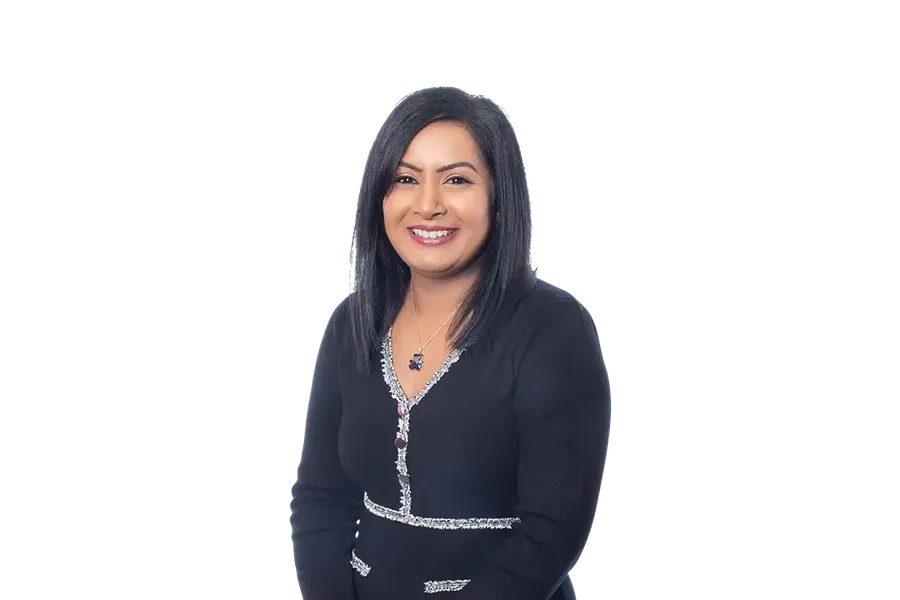 Arti Dhamu standing and smiling with long black hair in a black dress with silver trim, with a plain white background.