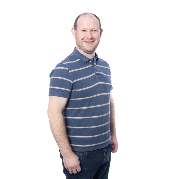 Smiling man in a blue striped polo shirt and jeans against a blurred background.