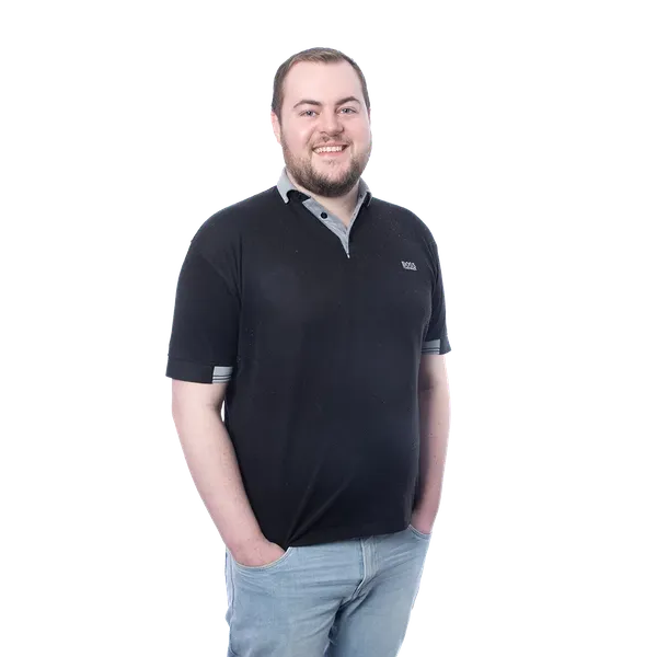 Man with short hair wearing a black polo shirt and jeans, smiling with hands in pockets, on a light blue and white gradient background.