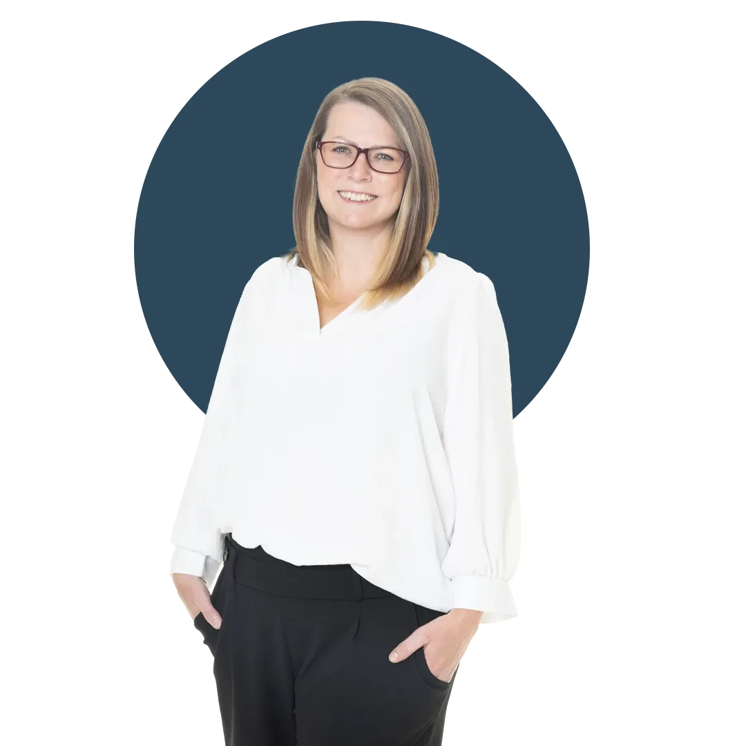 Lynsey Seymour, wearing a white blouse and black trousers, stands smiling against a dark blue background.