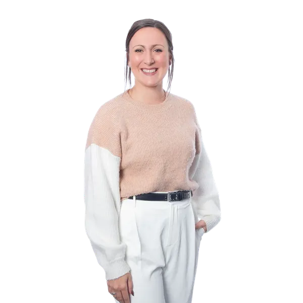 Smiling person wearing a beige and white sweater with white trousers, hands in pockets