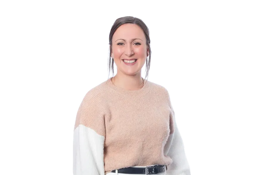 Smiling person wearing a beige and white sweater with white trousers, hands in pockets